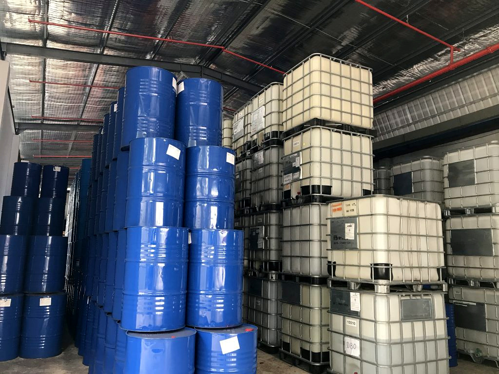 Stacked blue chemical drums and IBC containers in a warehouse