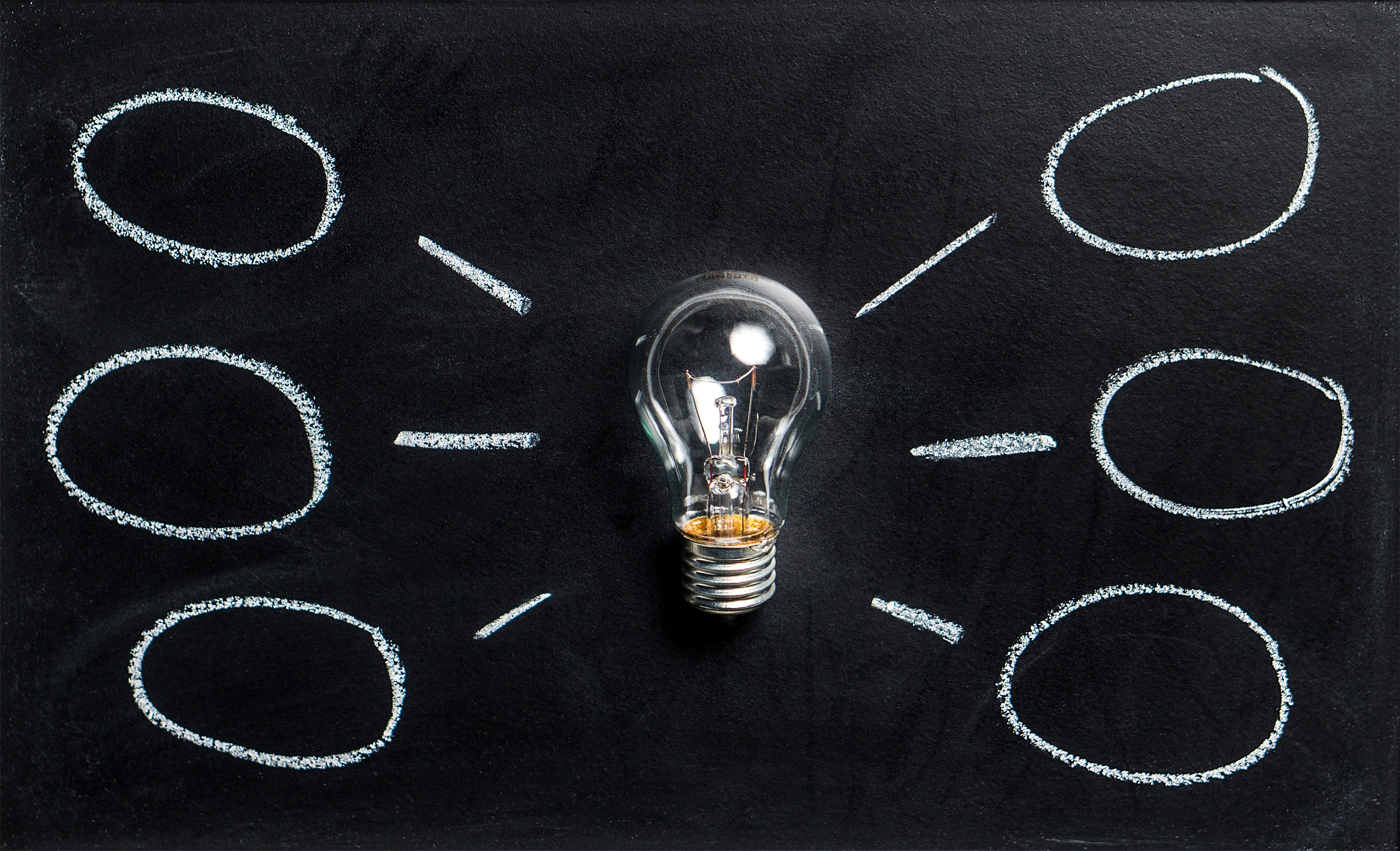 Light bulb drawn on a chalkboard, surrounded by empty idea bubbles